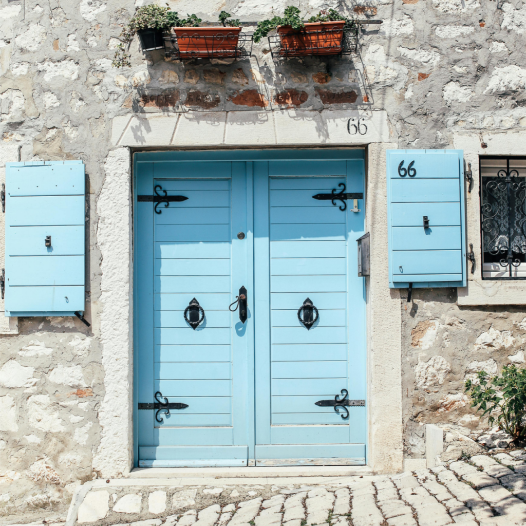 Une façade en pierre avec des doubles portes bleu clair et des volets assortis, récemment repeints